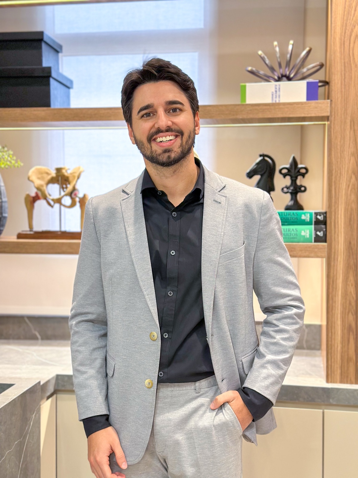 Dr. Guilherme Novato sorrindo em pé no consultório